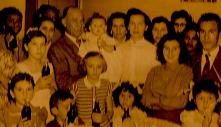 Em uma festa nos anos 50, Joaquim segura uma neta; Amélia está de camisa branca ao centro. Por que tão sérios?